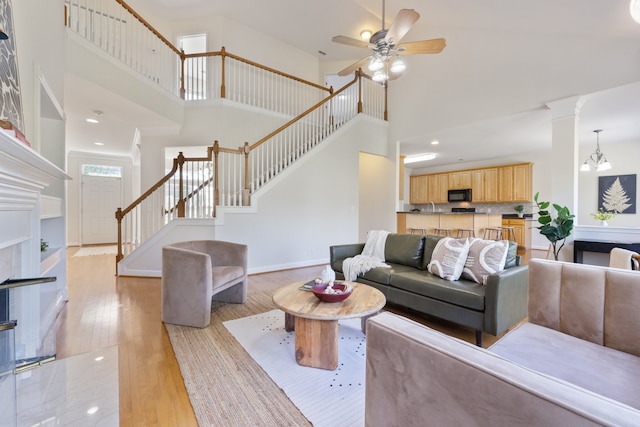 living room with a towering ceiling, ceiling fan with notable chandelier, and light hardwood / wood-style flooring