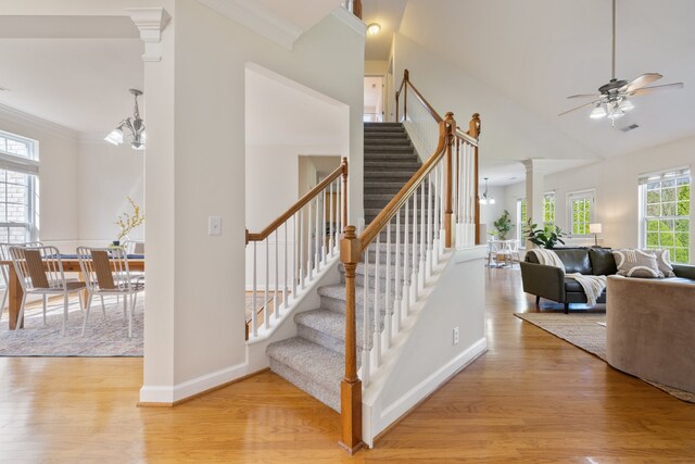 stairs with ornate columns, ceiling fan with notable chandelier, crown molding, and hardwood / wood-style floors