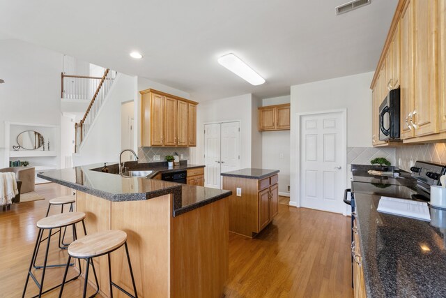 kitchen with kitchen peninsula, sink, light hardwood / wood-style flooring, black appliances, and decorative backsplash