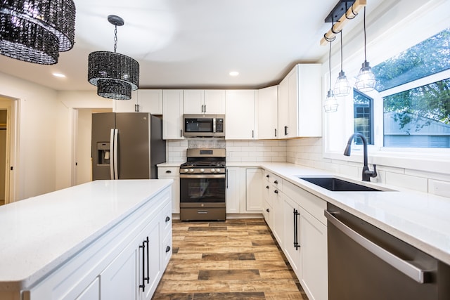 kitchen with white cabinetry, sink, stainless steel appliances, an inviting chandelier, and pendant lighting