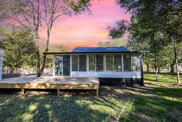 back house at dusk with a sunroom and a deck