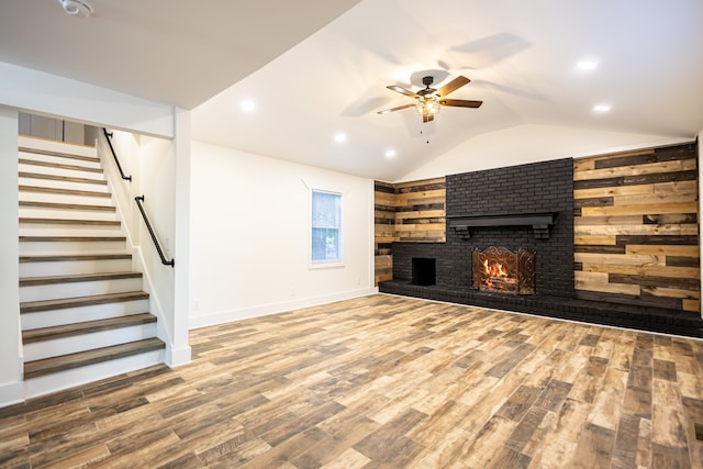 unfurnished living room with wood walls, vaulted ceiling, hardwood / wood-style flooring, ceiling fan, and a brick fireplace