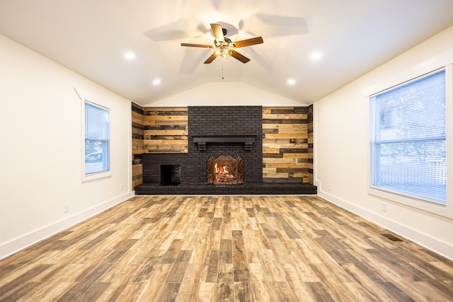 unfurnished living room featuring hardwood / wood-style flooring, ceiling fan, lofted ceiling, and a brick fireplace