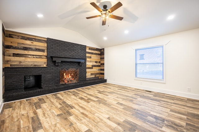 unfurnished living room featuring lofted ceiling, wooden walls, ceiling fan, a fireplace, and wood-type flooring