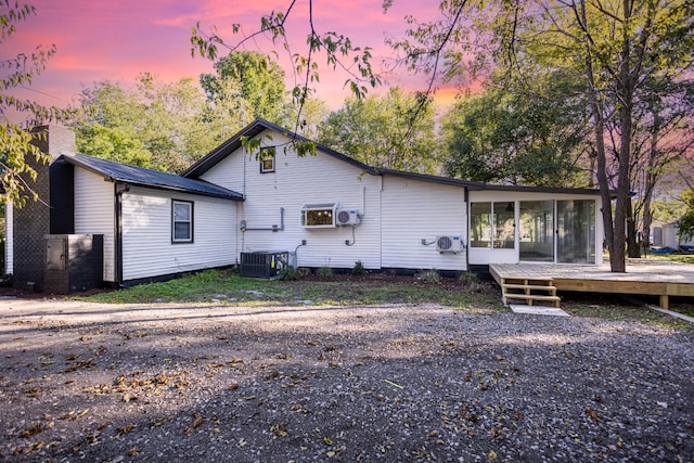 back house at dusk featuring a wooden deck, cooling unit, and a sunroom