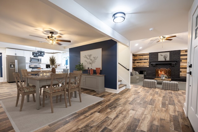 dining space with ceiling fan, hardwood / wood-style floors, vaulted ceiling, and a brick fireplace