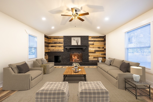 living room with ceiling fan, wood walls, vaulted ceiling, and a brick fireplace