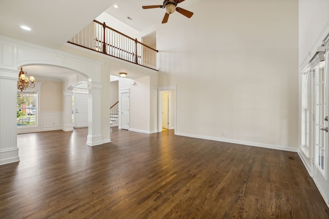 unfurnished living room featuring a high ceiling, ceiling fan, ornate columns, and dark hardwood / wood-style flooring