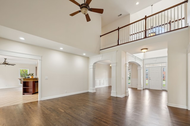 unfurnished living room featuring hardwood / wood-style floors, ceiling fan, a high ceiling, and decorative columns