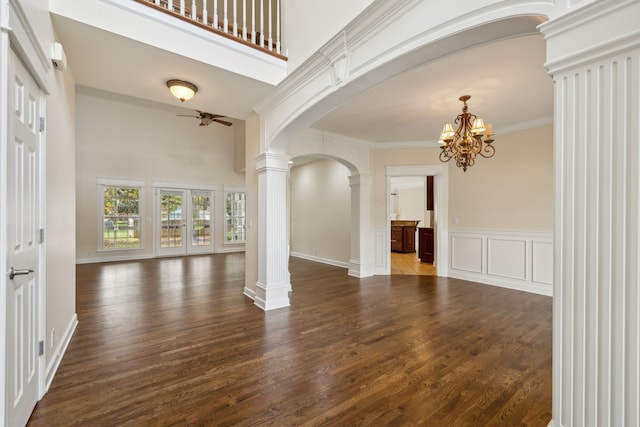 interior space featuring a high ceiling, ornamental molding, ceiling fan with notable chandelier, decorative columns, and dark hardwood / wood-style flooring