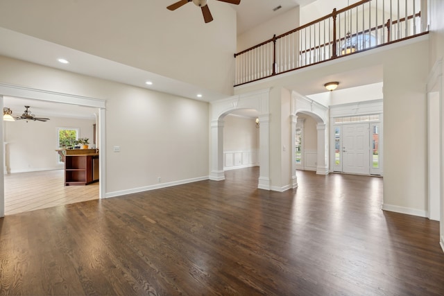 unfurnished living room with a high ceiling, ornate columns, ceiling fan, and dark hardwood / wood-style floors