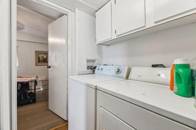 clothes washing area featuring dark wood-type flooring, washing machine and clothes dryer, and cabinets