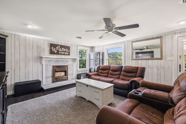 living room featuring a fireplace, ceiling fan, and wood walls