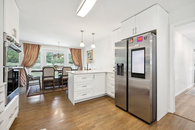 kitchen featuring kitchen peninsula, hanging light fixtures, appliances with stainless steel finishes, and white cabinetry