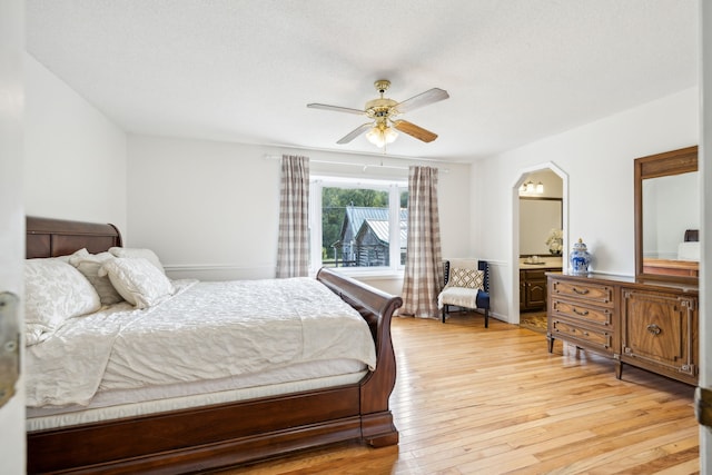 bedroom featuring light wood-type flooring, ceiling fan, ensuite bathroom, and a textured ceiling