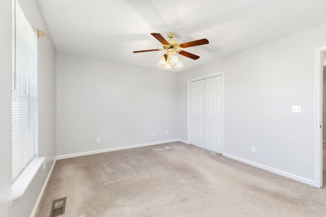 unfurnished bedroom with a closet, light carpet, a textured ceiling, and ceiling fan