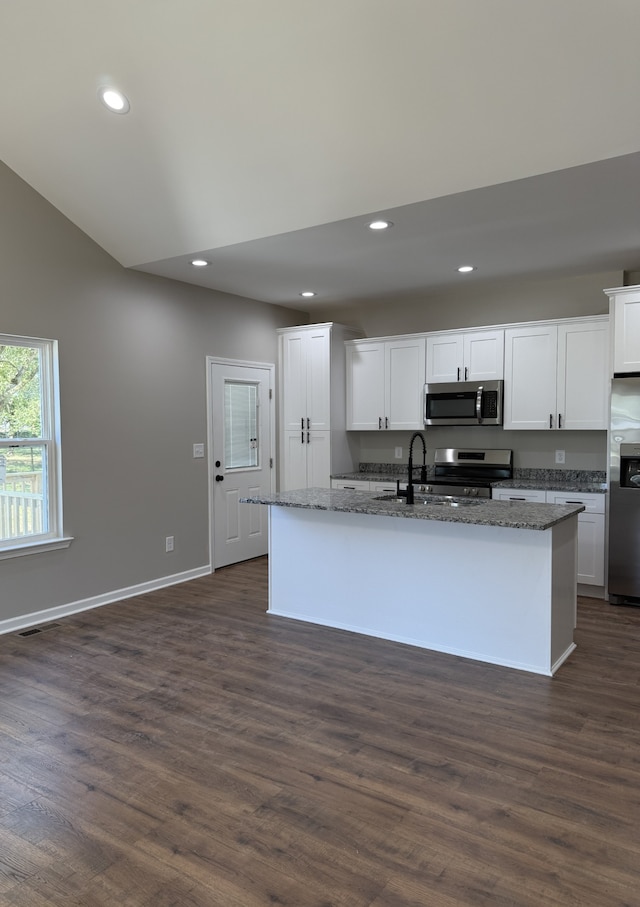 kitchen featuring an island with sink, stainless steel appliances, white cabinets, dark wood-type flooring, and dark stone counters