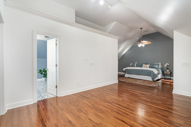 bedroom featuring track lighting, hardwood / wood-style floors, and vaulted ceiling