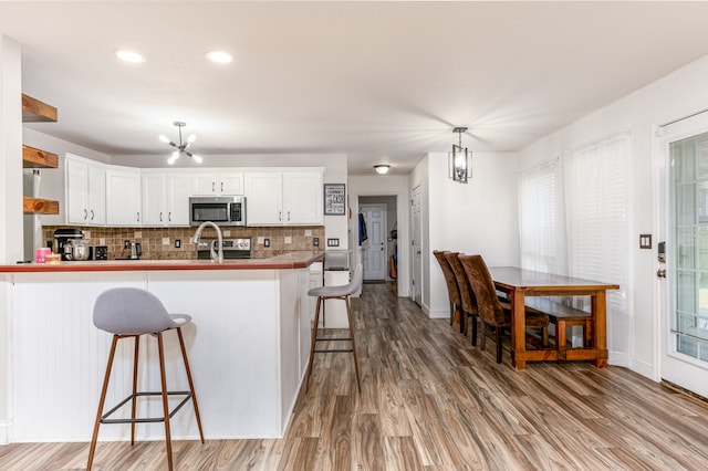 kitchen with a breakfast bar area, white cabinets, hanging light fixtures, and kitchen peninsula