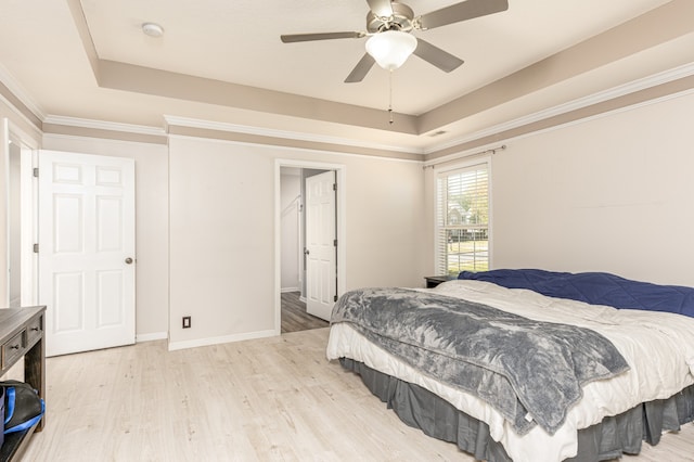 bedroom with ornamental molding, a tray ceiling, light hardwood / wood-style floors, and ceiling fan