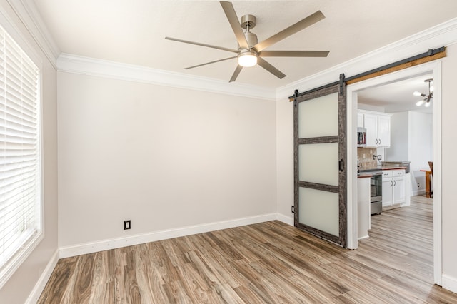 spare room with ornamental molding, light hardwood / wood-style flooring, a barn door, and ceiling fan