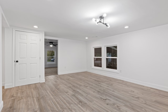 unfurnished room with ceiling fan with notable chandelier and light hardwood / wood-style flooring