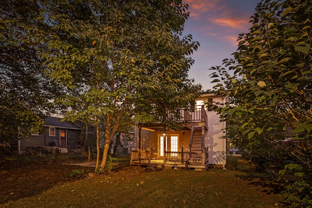 back house at dusk featuring a lawn, a wooden deck, and a balcony