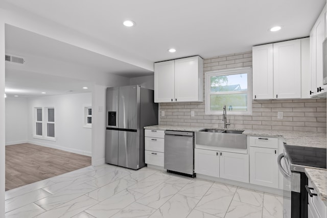 kitchen featuring light hardwood / wood-style flooring, light stone countertops, backsplash, appliances with stainless steel finishes, and white cabinetry