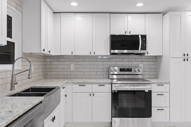 kitchen with tasteful backsplash, sink, light stone counters, stainless steel appliances, and white cabinetry