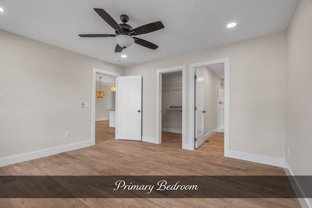 unfurnished bedroom featuring ceiling fan, a closet, light hardwood / wood-style floors, and a walk in closet