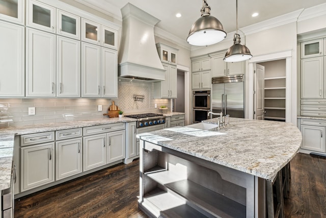 kitchen featuring a center island with sink, dark wood-type flooring, stainless steel appliances, custom range hood, and decorative backsplash