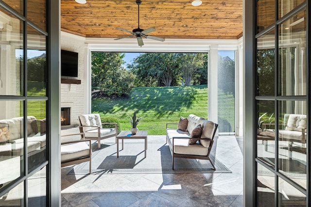 unfurnished sunroom featuring ceiling fan, an outdoor brick fireplace, and wood ceiling