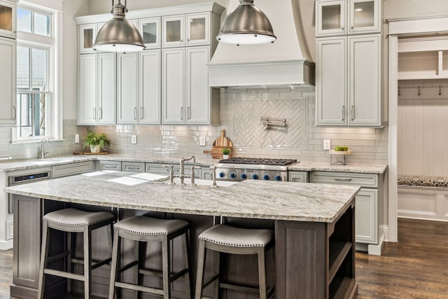 kitchen featuring light stone countertops, a kitchen island with sink, tasteful backsplash, dark hardwood / wood-style flooring, and a kitchen breakfast bar