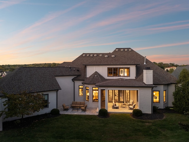 back house at dusk featuring an outdoor living space, a yard, and a patio