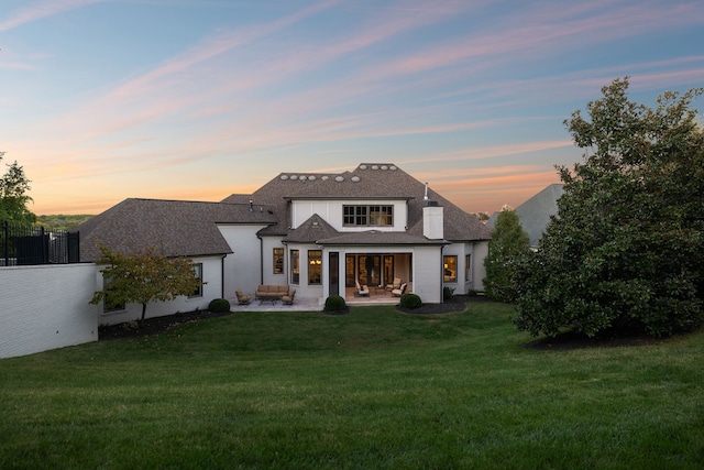 back house at dusk featuring a patio and a yard