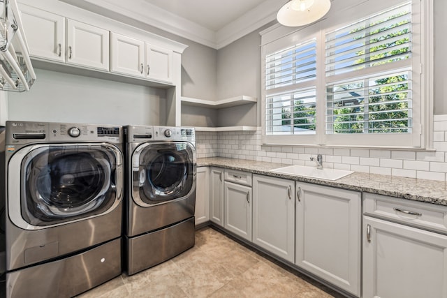 washroom with ornamental molding, cabinets, sink, and washing machine and clothes dryer