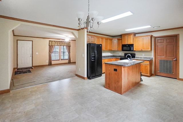 kitchen with decorative light fixtures, ornamental molding, black appliances, and an island with sink