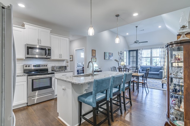 kitchen with ceiling fan, stainless steel appliances, sink, white cabinetry, and vaulted ceiling