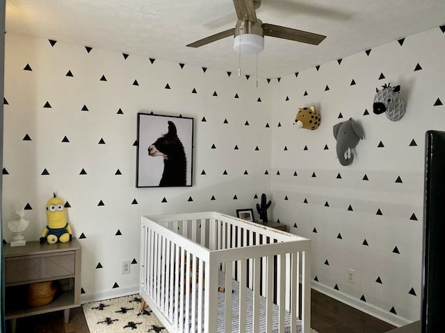 bedroom with a textured ceiling, hardwood / wood-style floors, a nursery area, and ceiling fan