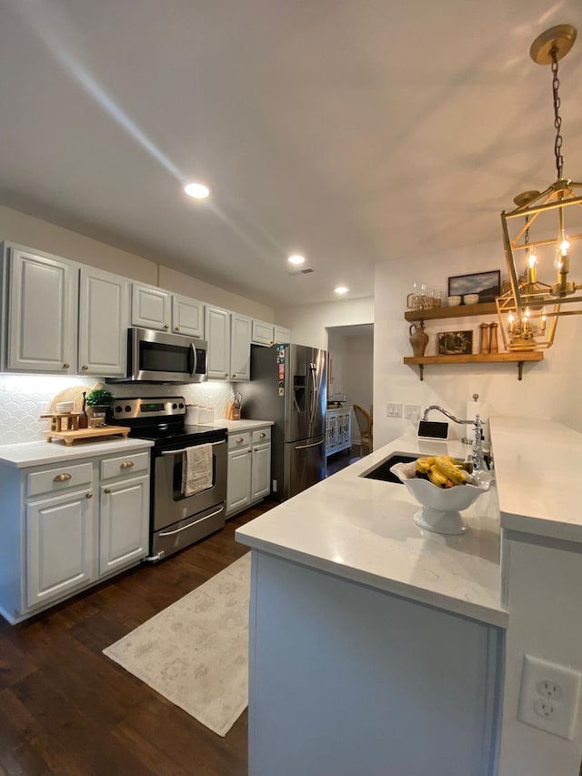 kitchen with kitchen peninsula, hanging light fixtures, white cabinets, and appliances with stainless steel finishes