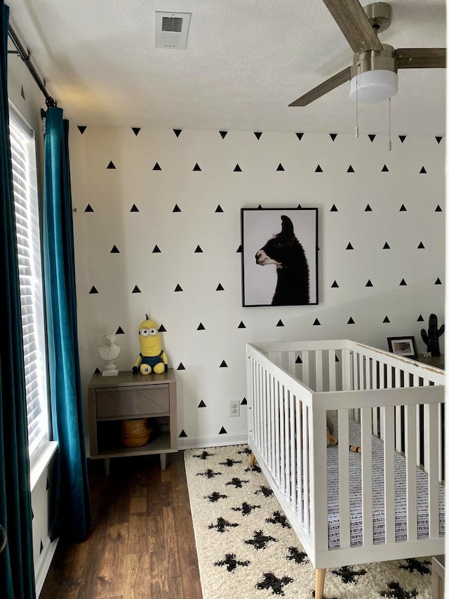 bedroom featuring a nursery area, multiple windows, ceiling fan, and dark hardwood / wood-style floors