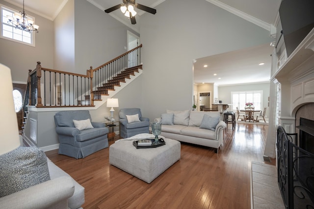 living room with high vaulted ceiling, wood-type flooring, ceiling fan with notable chandelier, crown molding, and a tiled fireplace