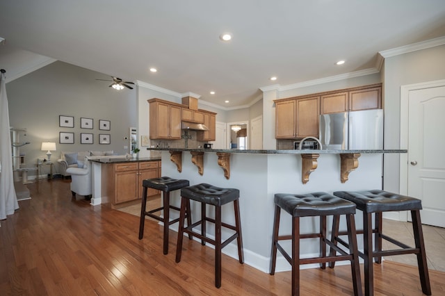 kitchen with stainless steel refrigerator, crown molding, a breakfast bar, kitchen peninsula, and hardwood / wood-style flooring