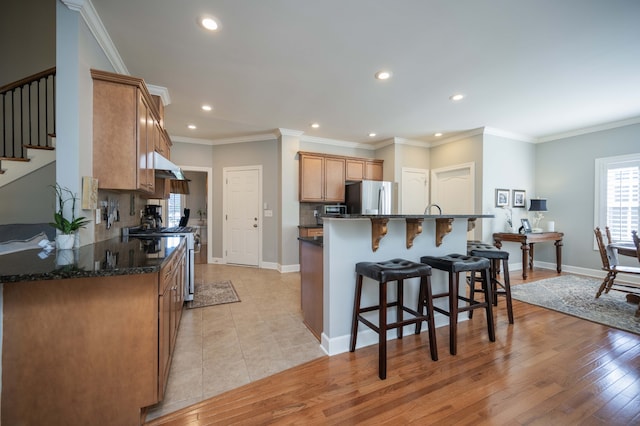 kitchen with appliances with stainless steel finishes, light wood-type flooring, crown molding, and backsplash