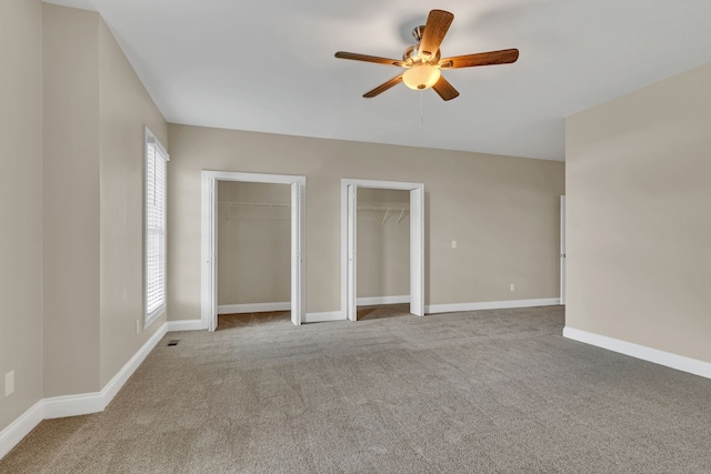 unfurnished bedroom featuring light colored carpet, multiple closets, multiple windows, and ceiling fan