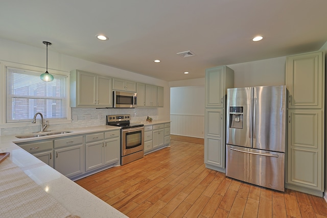 kitchen with light hardwood / wood-style flooring, hanging light fixtures, sink, backsplash, and appliances with stainless steel finishes