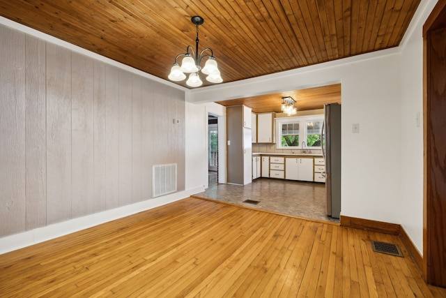 unfurnished dining area featuring wood walls, light hardwood / wood-style floors, wooden ceiling, and a notable chandelier