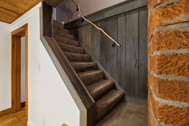 stairs featuring wood-type flooring, ornamental molding, wood ceiling, and wooden walls