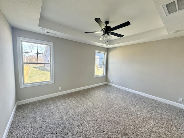 carpeted empty room featuring ceiling fan and a raised ceiling