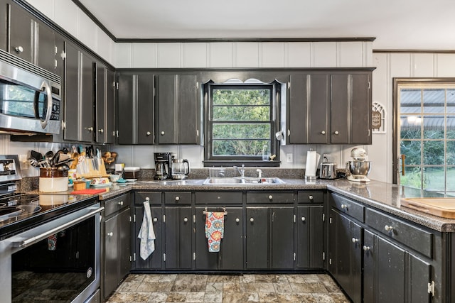 kitchen with dark stone countertops, stainless steel appliances, crown molding, and sink